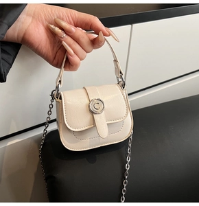 Detail of a creamy white mini saddle bag with C-shaped silver clasp and chain strap