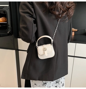 Detail of a white mini square crossbody bag with silver buckle on a black suit jacket