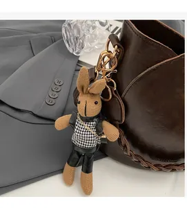 Detail of bunny plush charm with houndstooth vest and leather vest on a brown bag