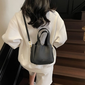 Classic black litchi pattern leather bucket bag shown as a crossbody on a staircase