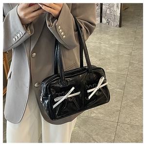 Close-up of black patent leather tote bag with silver bows and pleated pocket details