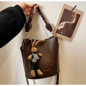 Detail of dark brown leather bucket bag with woven handle and knit rabbit charm accessory