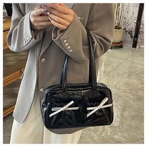 Close-up of stylish black patent leather tote bag featuring shiny silver bow decorations