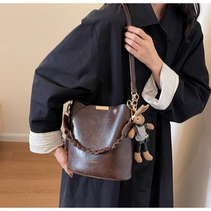 Detail of dark brown vintage bucket bag featuring a plush rabbit charm and dual straps