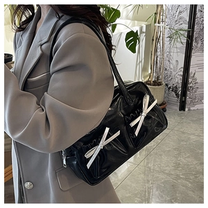 Detail of black glossy tote bag with silver bow accents worn with a grey blazer
