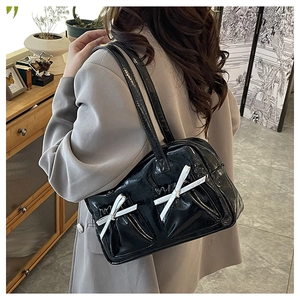 Detailed side view of a black patent leather shoulder bag with white bows on a model