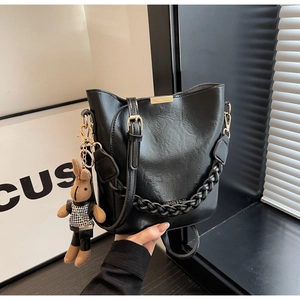 Detail of black leather bucket bag featuring woven chain strap and cute rabbit pendant