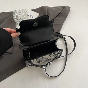 Floral print crossbody bag with black leather flap and thin strap on a gray blazer