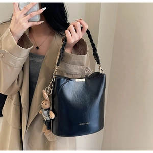 Close-up of black leather bucket bag with braided strap and plush rabbit pendant