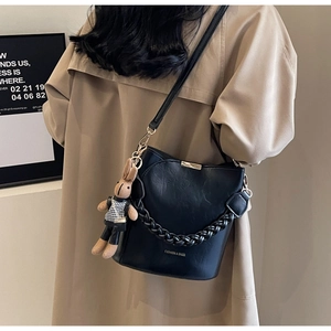 Close-up of black bucket bag featuring litchi leather texture and woven chain strap