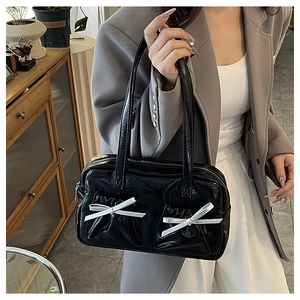 Detail of black glossy shoulder bag with white satin bows on the side view