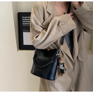 Detail of black leather bucket bag with woven handle and cute bear charm accessory