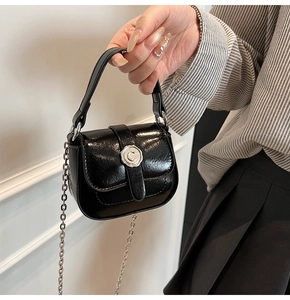 Detail of a black patent leather saddle bag featuring a silver floral buckle and chain