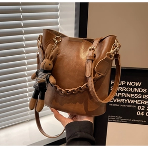 Detail of brown PU leather bucket bag with woven chain and rabbit pendant decoration