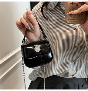 Close-up of black patent leather mini bag with silver C buckle and metal chain strap