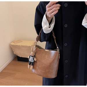 Detail of brown leather bucket bag with woven handle and plaid rabbit plush pendant