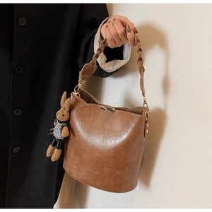 Detail of vintage brown leather bucket bag with woven handle and plaid rabbit charm