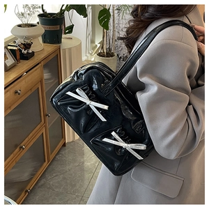 Detail of glossy black tote bag with double bow accents worn on a model's shoulder