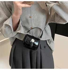 Detail of a mini black patent leather bag with a silver flower clasp and metal chain strap
