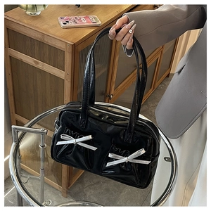 Detail of glossy black patent leather tote with silver bow charms and pleated pockets