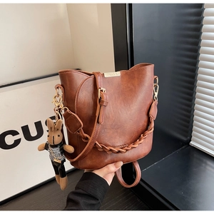 Vintage brown leather bucket bag with woven handle and cute bunny charm on white background