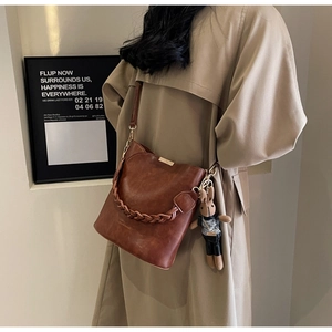 Detail of caramel leather bucket bag with woven handle and cute rabbit doll charm accessory