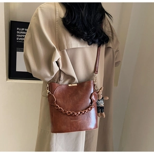 Back view of model in beige trench coat carrying a retro dark brown leather bucket bag