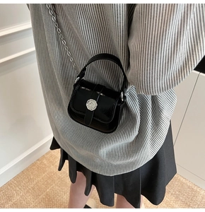 Close-up of a mini black glossy crossbody bag with silver chain and metal buckle detail