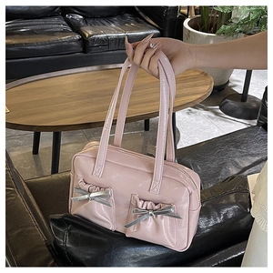 Detailed view of pink glossy tote bag with dual bow pockets on a black leather sofa