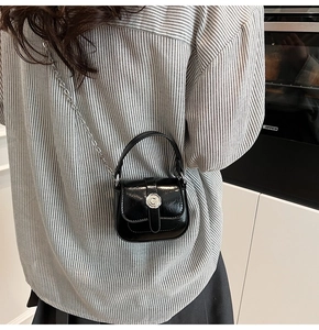 Detail of a mini black patent leather bag with a floral silver buckle and chain strap