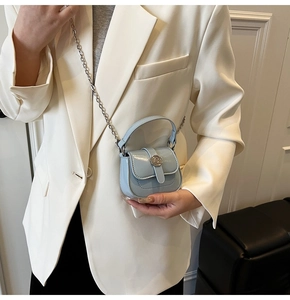 Light blue mini leather crossbody bag with metal chain strap worn on a white suit jacket