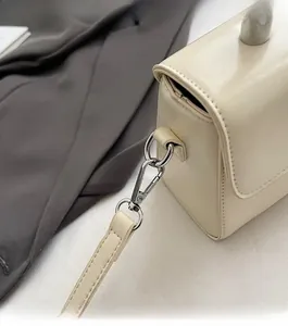Vue détaillée des ferrures argentées et des coutures du sac carré de couleur crème