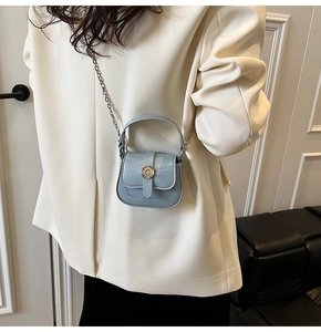 Close-up of a mini light blue patent leather crossbody bag with silver chain on a model