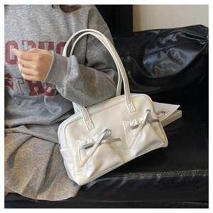 Detail of white patent leather shoulder bag with silver bows on a grey sweatshirt