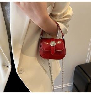Detail of a mini red patent leather saddle bag with silver C-logo buckle and chain strap