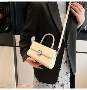 Détail d'un sac à main beige avec boucle argentée porté sur une veste de costume noire