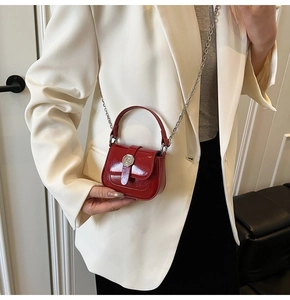 Close-up of a burgundy patent leather mini bag featuring a circular metal buckle and chain