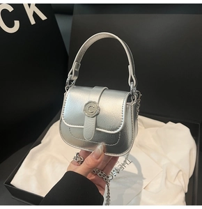 Detail of silver mini saddle bag with metallic finish and C-buckle on brand packaging