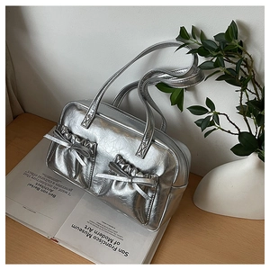 Detail of silver metallic tote bag with bow front pockets on a wooden table setup