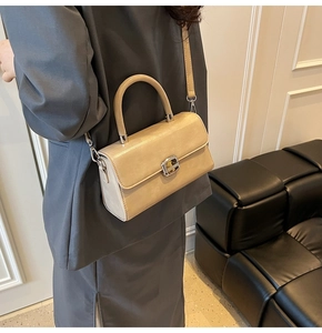 Détail d'un sac à main beige élégant avec boucle dorée porté par mannequin en costume