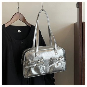 Detail of silver metallic tote bag featuring dual front pockets and delicate bow accents