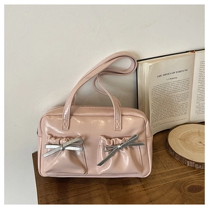 Detailed view of pink patent leather tote bag with silver bow accents on wooden desk