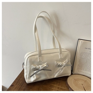 Detail of white glossy tote bag featuring pleated front pockets and silver bow accents
