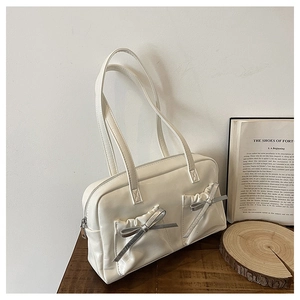 Detail of cream white tote bag with glossy finish and silver bow accents on front pockets