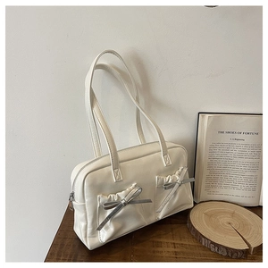 Detail of white glossy leather tote bag featuring two front pockets and silver bow accents