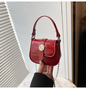 Detail of red patent leather mini bag featuring glossy texture and gold C-buckle closure