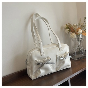 Detail of white tote bag with silver bow accents and pleated pockets on dark wood surface