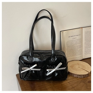 Detail of glossy black crinkled leather tote bag featuring silver bow accents and textures