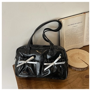 Detail of glossy black tote bag featuring silver bow accents and dual front pockets