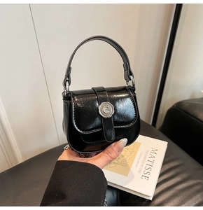 Detail view of black glossy leather mini saddle bag with vintage silver metal logo buckle